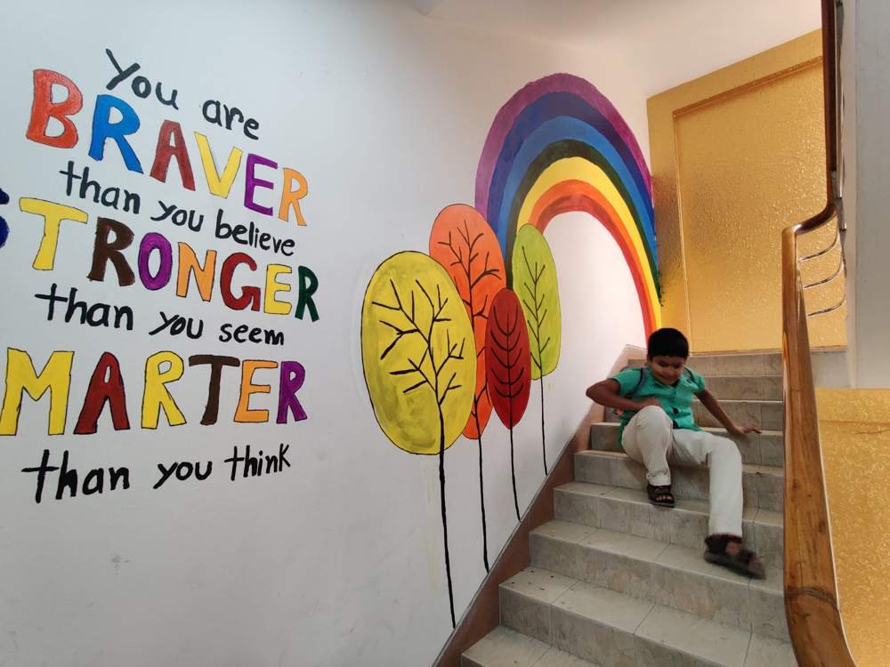 A colourful rainbow and trees mural on the stairs with an encouraging message